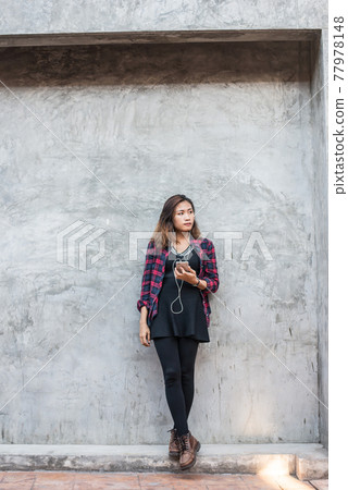 Portrait of handsome young hipster woman listening music with smartphone against a grunge bricks wall background. Portrait of handsome young hipster woman listening music with smartphone against a grunge bricks wall background. 77978148