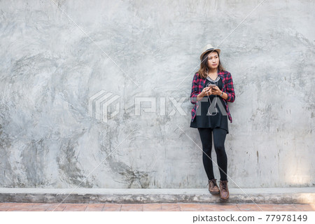 Portrait of handsome young hipster woman listening music with smartphone against a grunge bricks wall background. 77978149