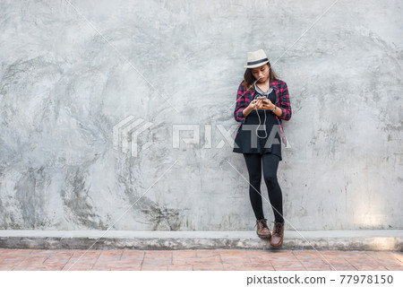 Portrait of handsome young hipster woman listening music with smartphone against a grunge bricks wall background. Portrait of handsome young hipster woman listening music with smartphone against a grunge bricks wall background. 77978150