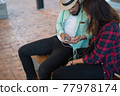Hipster couple listening music together while sitting on bench and enjoying in urban. 77978174
