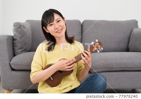 A woman playing the ukulele in front of the sofa 77978240