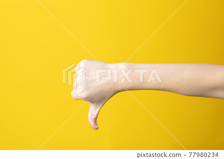 Hand in fist with thumb down gesture on yellow background. 77980234