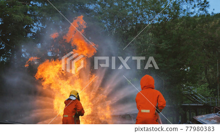 Firefighter fighting with flame using fire hose chemical water foam spray engine. Fireman wear hard hat, body safe suit uniform for protection. Rescue training in fire fighting extinguisher 77980383