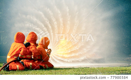 Firefighter fighting with flame using fire hose chemical water foam spray engine. Fireman wear hard hat, body safe suit uniform for protection. Rescue training in fire fighting extinguisher 77980384
