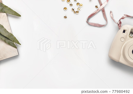 Pink camera, metallic push pins and green leaves of flower on magazine isolated on white. Modern technology and stationery. Close up, copy space 77980492