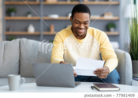 Smiling african american man reading letter at home Smiling african american man reading letter at home 77981409
