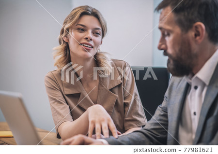 Cheerful young woman touching hand of serious male colleague 77981621