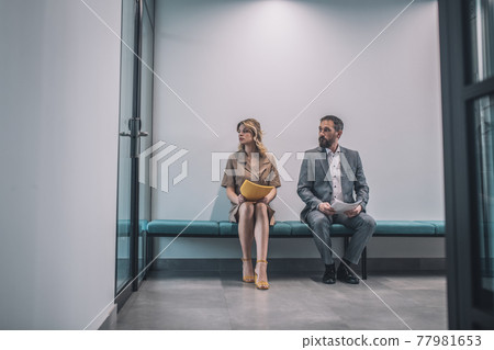 Man and woman with documents sitting in office corridor Man and woman with documents sitting in office corridor 77981653