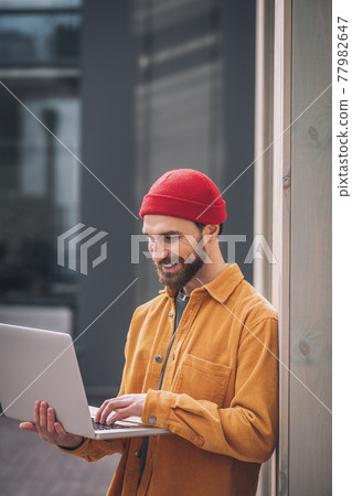 Bearded young man in a red hat with a laptop 77982647