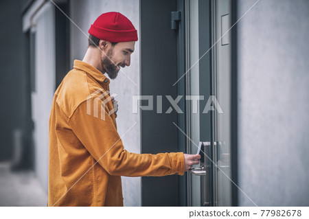 Bearded young man opening the door with an access card Bearded young man opening the door with an access card 77982678