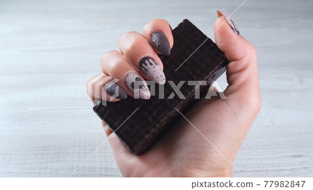 Female hand with beautiful manicure nails in the form of chocolate candies, holding an unrolled bar 77982847