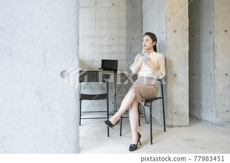 A young woman sitting in a chair in a fashionable office and looking at her smartphone with her legs crossed 77983451