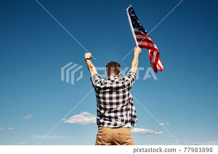 Man holds usa national flag against blue sky Man holds usa national flag against blue sky 77983898