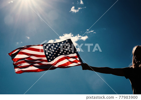 Woman holds usa flag against blue sky Woman holds usa flag against blue sky 77983900