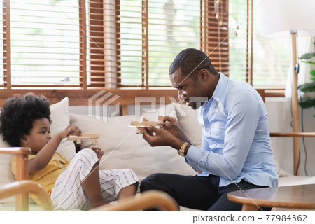 Cheerful African American Father playing airplane toys with his little son on sofa at home. Cheerful African American Father playing airplane toys with his little son on sofa at home. 77984362