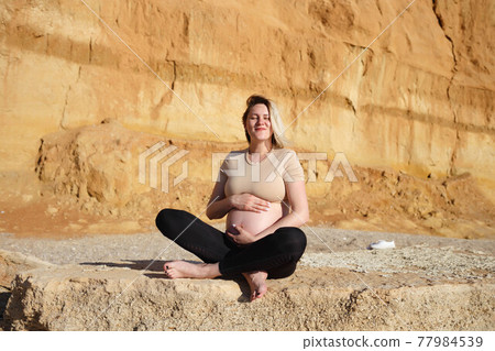 pregnant woman sitting on yellow rock and meditating 77984539