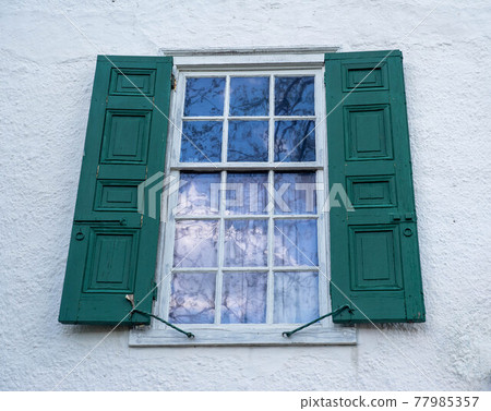 fifteen pane colonial window with green shutters reflecting blue sky and clouds fifteen pane colonial window with green shutters reflecting blue sky and clouds 77985357