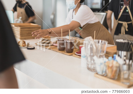 Selected focus on iced chocolate in plastic cup with waitress in background. 77986003