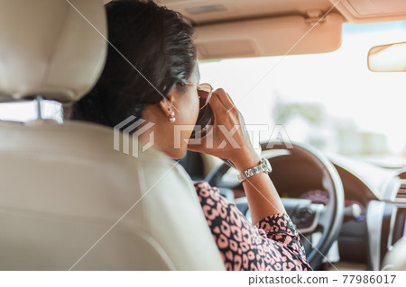 Asian woman drinking hot coffee from vacuum flask while driving a car. Asian woman drinking hot coffee from vacuum flask while driving a car. 77986017