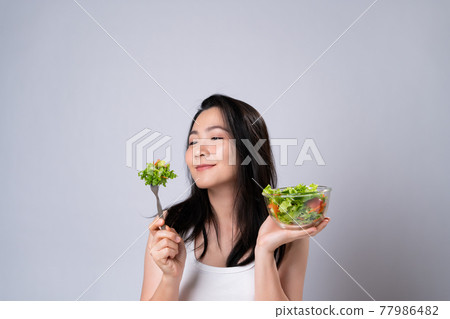 Asian woman eating salad isolated over white background. Asian woman eating salad isolated over white background. 77986482