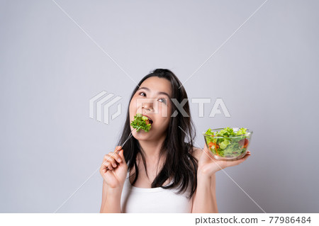 Asian woman eating salad isolated over white background. Asian woman eating salad isolated over white background. 77986484