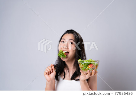 Asian woman eating salad isolated over white background. Asian woman eating salad isolated over white background. 77986486