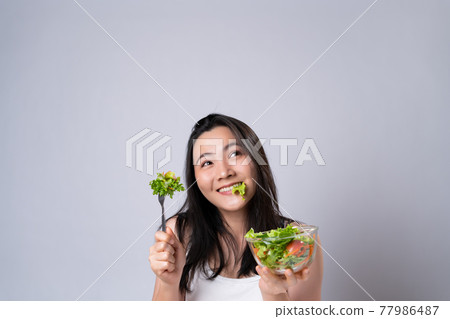 Asian woman eating salad isolated over white background. Asian woman eating salad isolated over white background. 77986487