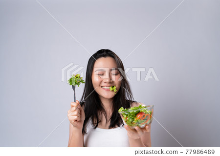 Asian woman eating salad isolated over white background. Asian woman eating salad isolated over white background. 77986489
