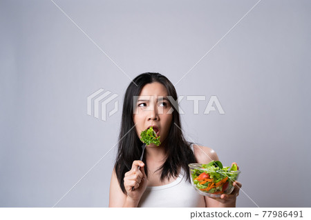 Asian woman confused with eating salad isolated over white background. Asian woman confused with eating salad isolated over white background. 77986491