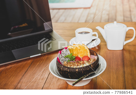 Healthy smoothie bowl of breakfast with laptop on wooden table. 77986541
