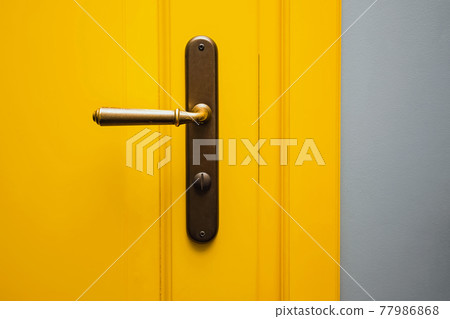 Yellow door with a bronze door handle close-up. Yellow door with a bronze door handle close-up. 77986868