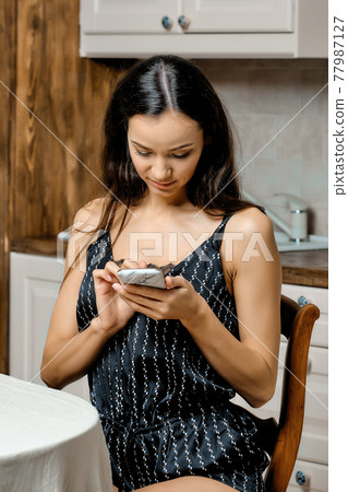Woman scrolling feed on smartphone in the kitchen 77987127