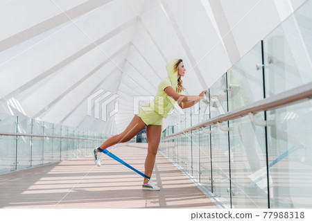 A sporty girl does resistance band exercises outdoors. Sports training for girls 77988318