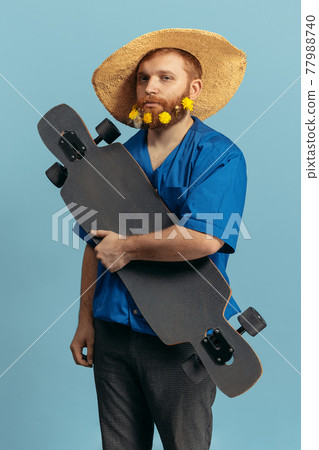 Young red headed and bearded man in straw hat standing isolated over blue bacground. Eras comparison 77988740