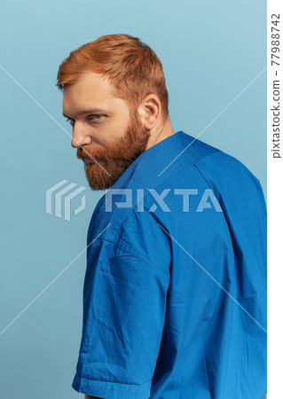 Close-up portrait of young red headed and bearded man isolated over blue bacground. Eras comparison 77988742