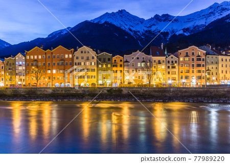 Panorama view of colorful buildings and mountains across from the flowing river of Innsbruck, Austria on a late evening night Panorama view of colorful buildings and mountains across from the flowing river of Innsbruck, Austria on a late evening night 77989220