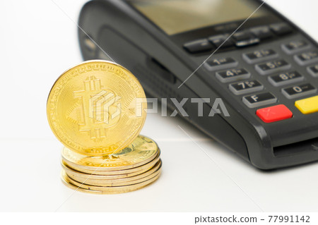 Golden bitcoin coins next to payment terminal on the table. Cryptocurrency for payment concept.  77991142