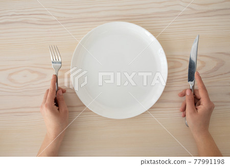 White empty plate and female hands holding silver fork and knife on wooden table background, top view White empty plate and female hands holding silver fork and knife on wooden table background, top view 77991198