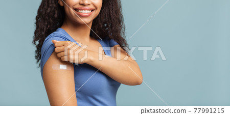 Successful covid-19 vaccination. Happy unrecognizable black woman showing arm with plaster, blue background, free space Successful covid-19 vaccination. Happy unrecognizable black woman showing arm with plaster, blue background, free space 77991215