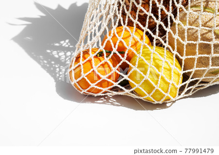 Tropical fruits in reusable shopping mesh bag. Detox fruit in string bag on the table. Healthy eating zero waste concept Tropical fruits in reusable shopping mesh bag. Detox fruit in string bag on the table. Healthy eating zero waste concept 77991479
