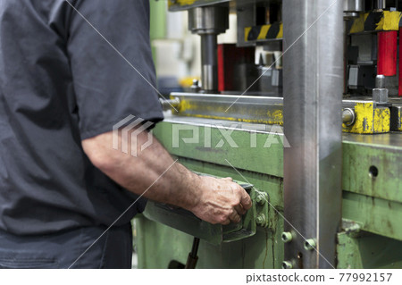 Steel Manufacturing Plant. A Worker is Placing a Piece of Metal Inside the Press. The Press is 77992157