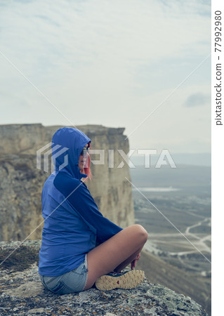 Woman sits on a rock, looking at the landscape and enjoying the view and fresh air. 77992980