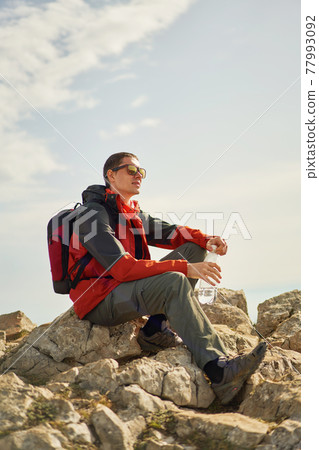 Man sits on a rock, looking at the landscape and enjoying the view and fresh air. Man sits on a rock, looking at the landscape and enjoying the view and fresh air. 77993092