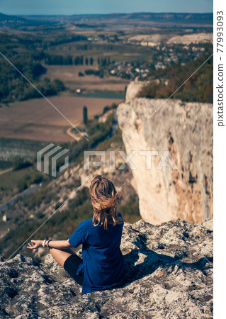 Young woman sits on a rock, looking at the landscape and enjoying the view and fresh air. Young woman sits on a rock, looking at the landscape and enjoying the view and fresh air. 77993093