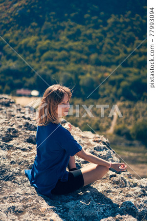 Young woman sits on a rock, looking at the landscape and enjoying the view and fresh air. Young woman sits on a rock, looking at the landscape and enjoying the view and fresh air. 77993094