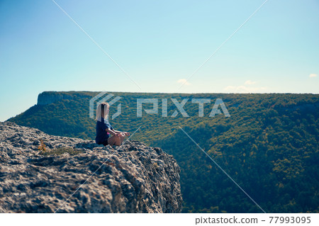 Young woman sits on a rock, looking at the landscape and enjoying the view and fresh air. Young woman sits on a rock, looking at the landscape and enjoying the view and fresh air. 77993095