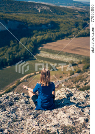 Young woman sits on a rock, looking at the landscape and enjoying the view and fresh air. Young woman sits on a rock, looking at the landscape and enjoying the view and fresh air. 77993096
