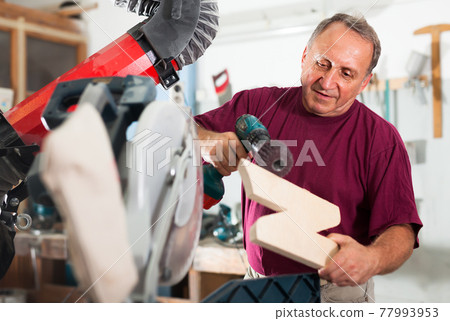 Worker grinds wooden 3d detail on grinding machine Worker grinds wooden 3d detail on grinding machine 77993953
