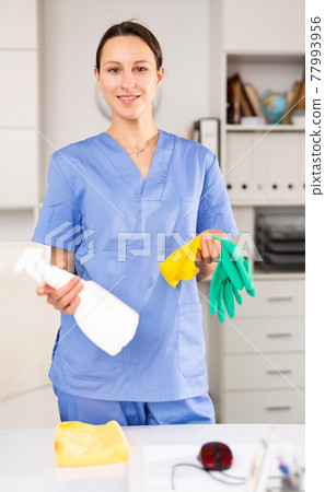 Cleaning lady of cleaning company wipes dust from table in office Cleaning lady of cleaning company wipes dust from table in office 77993956