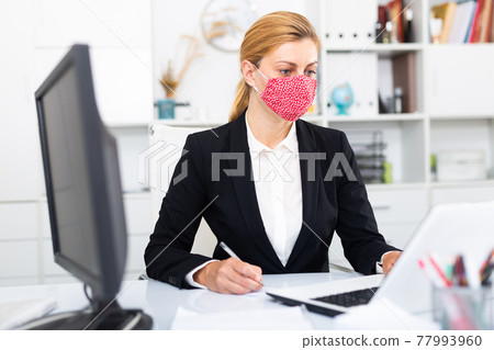 Woman in mask working at office 77993960